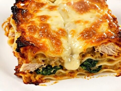 A top-down view of a slow cooker filled with raw chicken, spinach, artichoke, and creamy Alfredo sauce.