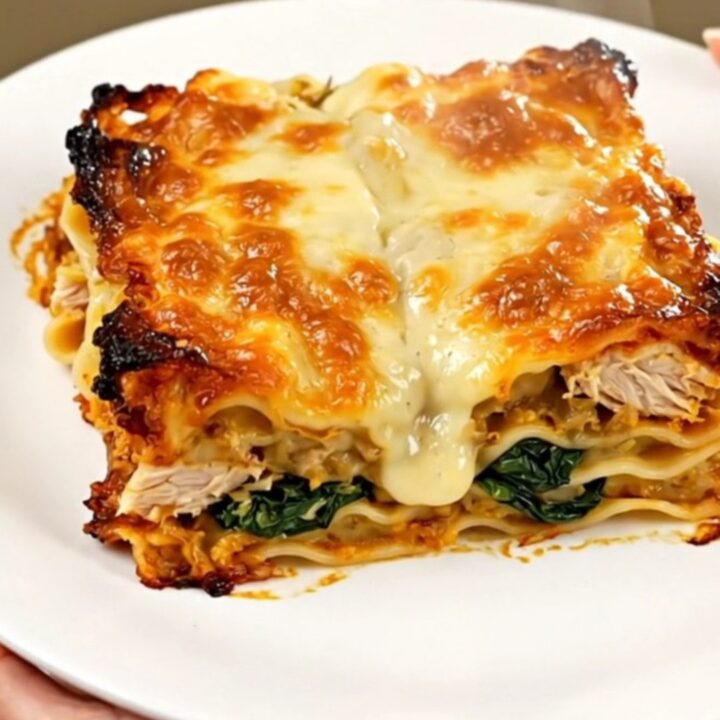 A top-down view of a slow cooker filled with raw chicken, spinach, artichoke, and creamy Alfredo sauce.