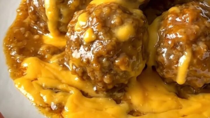 A close-up view of beef meatballs coated in a glossy, savory beer cheese sauce served on a white plate.