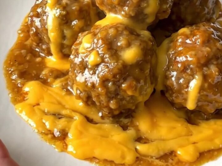 A close-up view of beef meatballs coated in a glossy, savory beer cheese sauce served on a white plate.