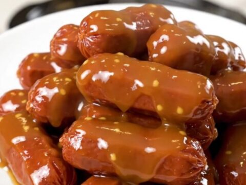 A slow cooker filled with glazed honey mustard cocktail smokies on a speckled countertop.