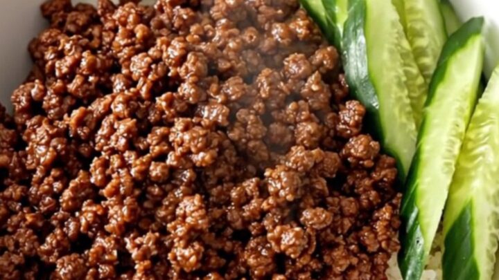 A close-up view of slow cooker Korean ground beef served over white rice with fresh cucumber slices in a white bowl.