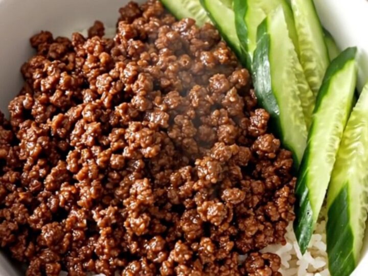 A close-up view of slow cooker Korean ground beef served over white rice with fresh cucumber slices in a white bowl.