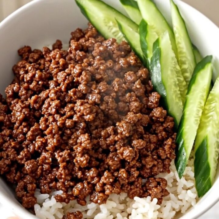A close-up view of slow cooker Korean ground beef served over white rice with fresh cucumber slices in a white bowl.