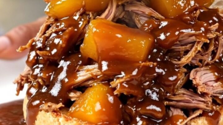 A close-up of a tender pulled pork sandwich with peach pieces on a toasted bun.
