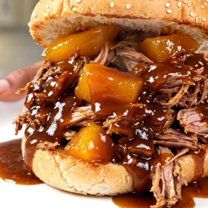 A close-up of a tender pulled pork sandwich with peach pieces on a toasted bun.