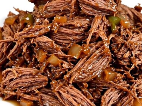 A close-up view of succulent shredded beef with poblano strips and red onions in a slow cooker.