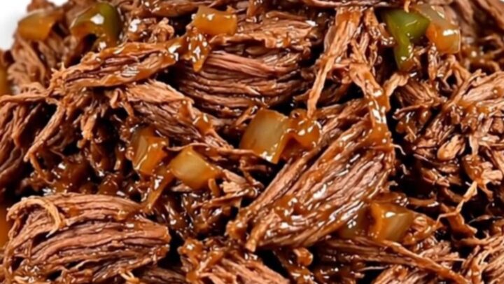 A close-up view of succulent shredded beef with poblano strips and red onions in a slow cooker.
