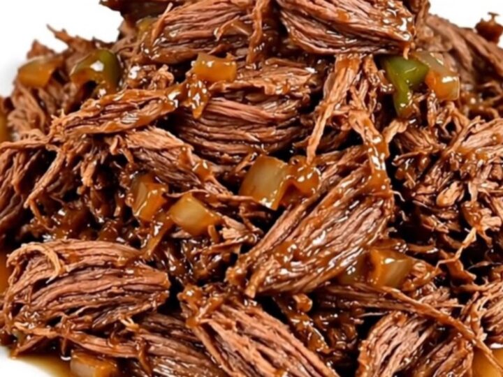 A close-up view of succulent shredded beef with poblano strips and red onions in a slow cooker.