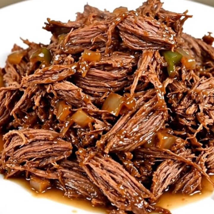 A close-up view of succulent shredded beef with poblano strips and red onions in a slow cooker.