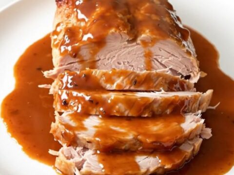 A close-up of a succulent, glazed turkey breast in a slow cooker topped with red bell peppers.