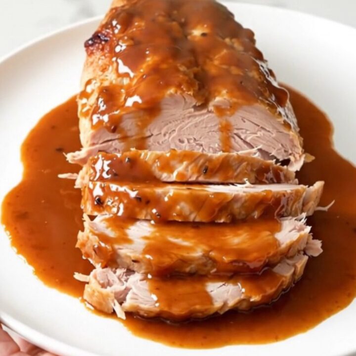 A close-up of a succulent, glazed turkey breast in a slow cooker topped with red bell peppers.