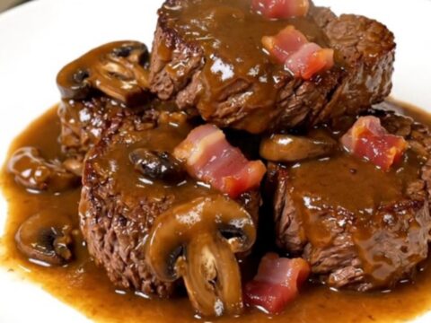 A close-up of tender, glossy beef chuck cubes served on a white plate with sautéed mushrooms and bacon.