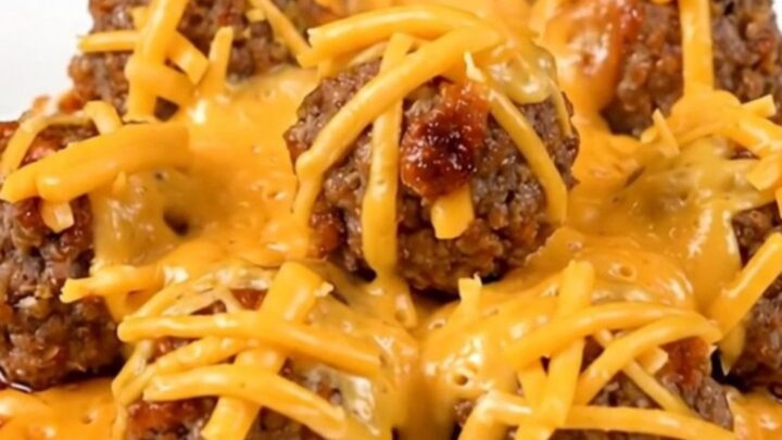 A plate of steaming hot slow cooker cheesy enchilada meatballs covered in melted cheese.