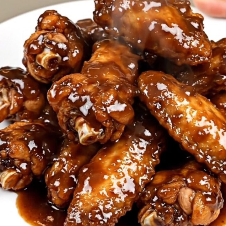 A close-up of glossy, smoky chipotle lime chicken wings on a white plate.