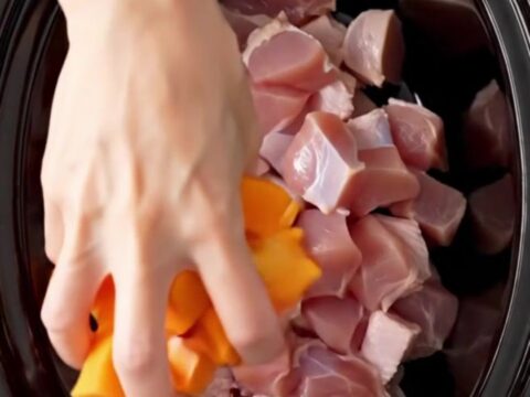 A top-down shot of a black slow cooker filled with cubed turkey, butternut squash, and cranberry sauce before cooking.