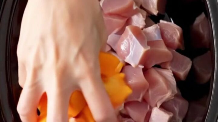 A top-down shot of a black slow cooker filled with cubed turkey, butternut squash, and cranberry sauce before cooking.