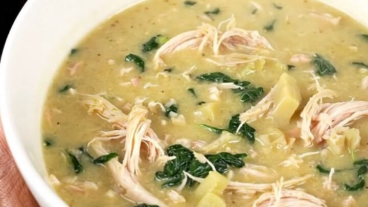 A steaming bowl of creamy spinach artichoke chicken soup with shredded chicken and visible spinach leaves.
