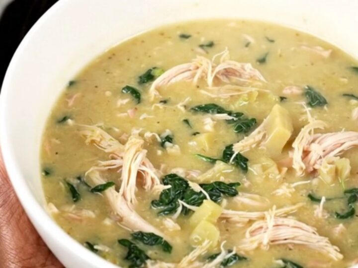 A steaming bowl of creamy spinach artichoke chicken soup with shredded chicken and visible spinach leaves.