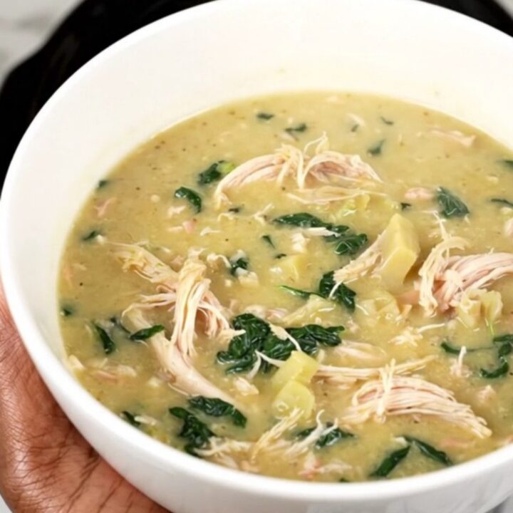 A steaming bowl of creamy spinach artichoke chicken soup with shredded chicken and visible spinach leaves.