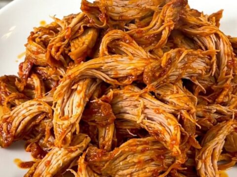 A slow cooker filled with tender, shredded pollo asado served on a white plate.