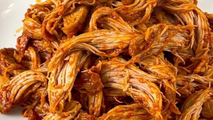 A slow cooker filled with tender, shredded pollo asado served on a white plate.