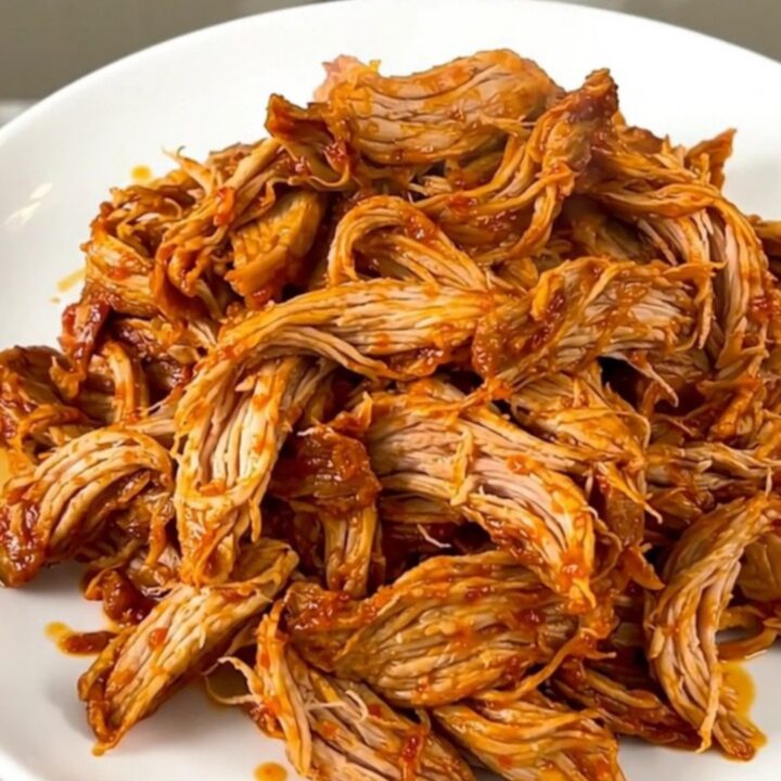 A slow cooker filled with tender, shredded pollo asado served on a white plate.