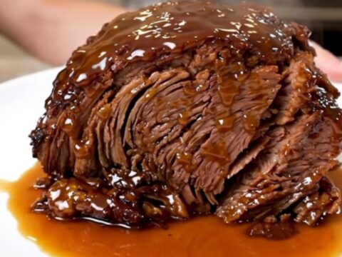 A close-up of a tender, glossy Crockpot Peach Bourbon Pot Roast served on a white plate.