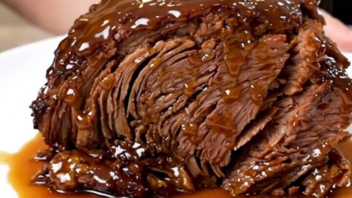 A close-up of a tender, glossy Crockpot Peach Bourbon Pot Roast served on a white plate.