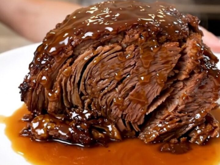 A close-up of a tender, glossy Crockpot Peach Bourbon Pot Roast served on a white plate.