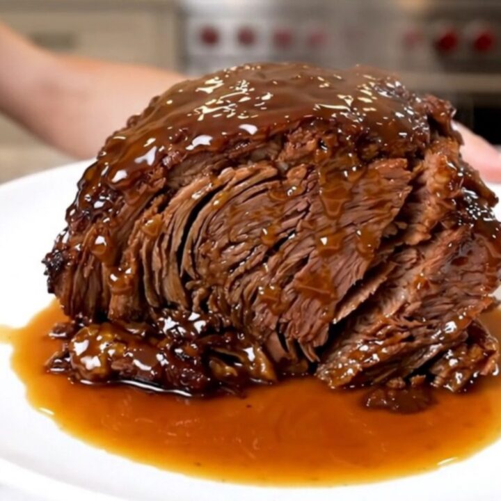 A close-up of a tender, glossy Crockpot Peach Bourbon Pot Roast served on a white plate.