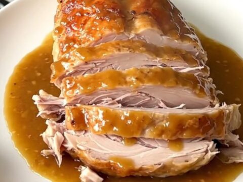 A cooked maple mustard turkey breast resting in a slow cooker with onions.