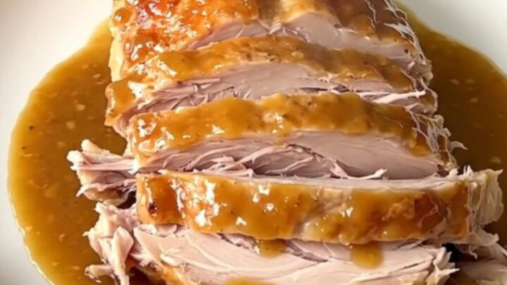 A cooked maple mustard turkey breast resting in a slow cooker with onions.