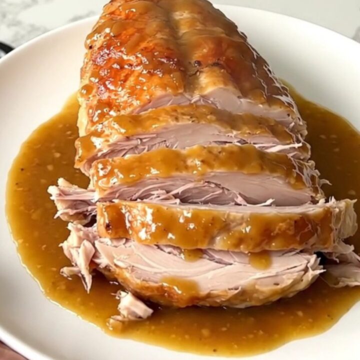 A cooked maple mustard turkey breast resting in a slow cooker with onions.