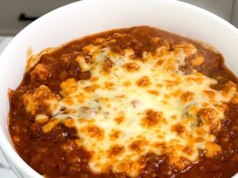 A white bowl filled with slow-cooked beef stew topped with melted cheddar cheese.