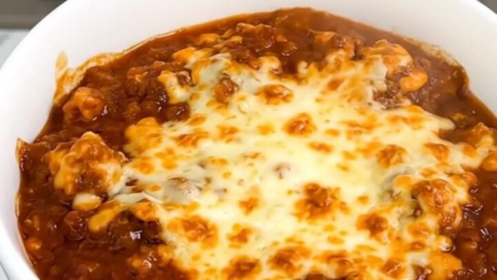 A white bowl filled with slow-cooked beef stew topped with melted cheddar cheese.