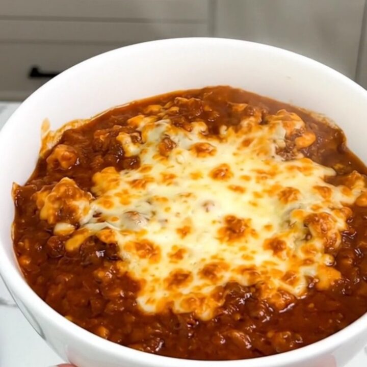 A white bowl filled with slow-cooked beef stew topped with melted cheddar cheese.