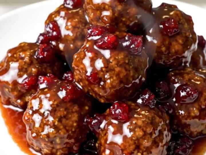 A black slow cooker filled with glazed meatballs on a white quartz countertop.
