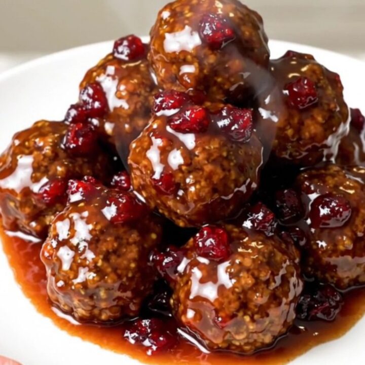 A black slow cooker filled with glazed meatballs on a white quartz countertop.