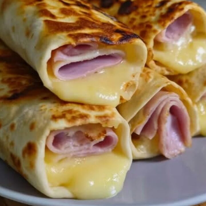 A stack of golden brown air fryer ham and cheese wraps on a white plate.