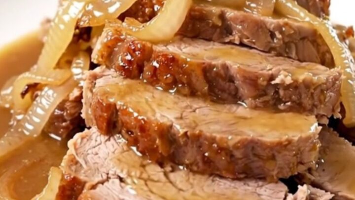 A tender, sliced Crockpot Sweet Onion Dijon Pork Roast served on a white plate with glossy onions.