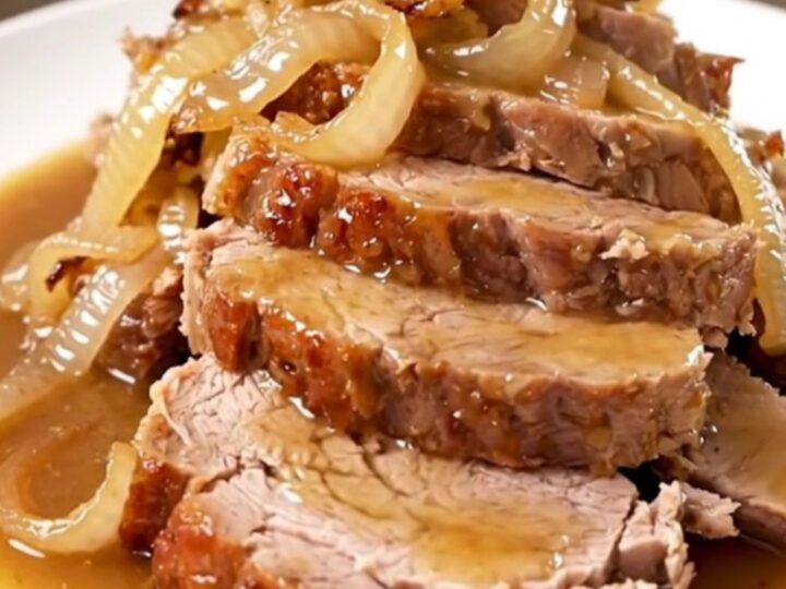 A tender, sliced Crockpot Sweet Onion Dijon Pork Roast served on a white plate with glossy onions.
