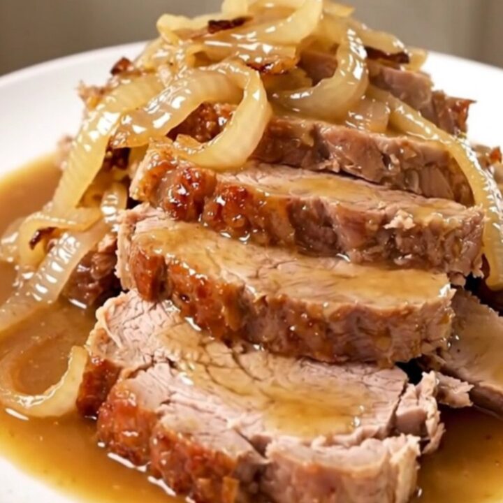 A tender, sliced Crockpot Sweet Onion Dijon Pork Roast served on a white plate with glossy onions.