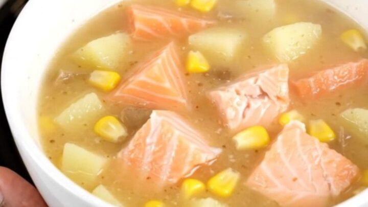 A steaming white bowl of creamy salmon corn chowder filled with chunks of pink salmon, yellow corn, and potatoes.