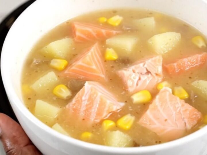 A steaming white bowl of creamy salmon corn chowder filled with chunks of pink salmon, yellow corn, and potatoes.