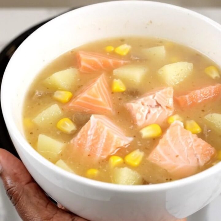 A steaming white bowl of creamy salmon corn chowder filled with chunks of pink salmon, yellow corn, and potatoes.