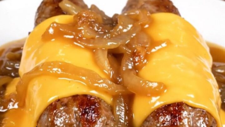 A close-up shot of juicy bratwurst links in a slow cooker topped with caramelized onions and melted provolone cheese.