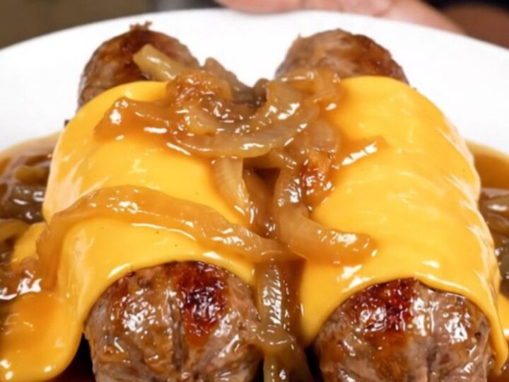 A close-up shot of juicy bratwurst links in a slow cooker topped with caramelized onions and melted provolone cheese.