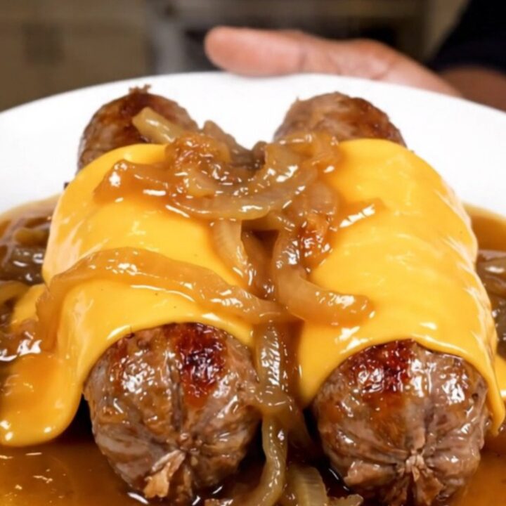 A close-up shot of juicy bratwurst links in a slow cooker topped with caramelized onions and melted provolone cheese.