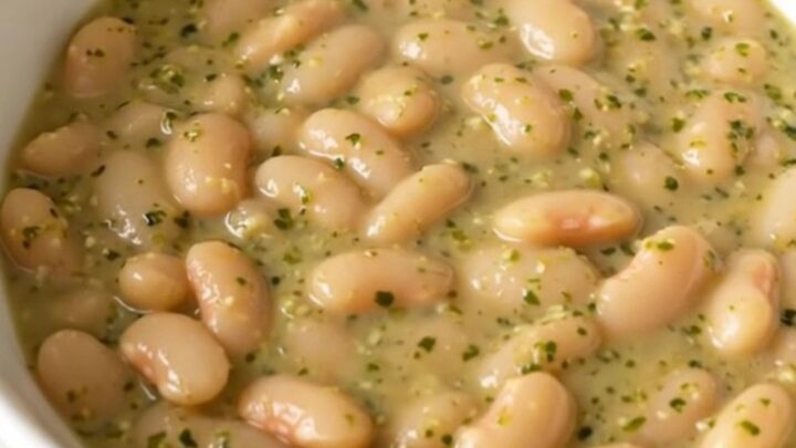 A top-down view of a slow cooker filled with white beans, chopped zucchini, and dollops of pesto and cream cheese.